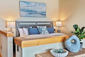 A bedroom with a bed, two bedside lamps, a wall-mounted painting, a bedside table with a lamp, and a decorative bowl.