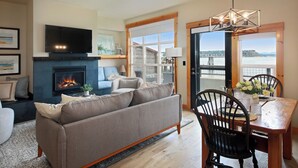 A living room with a fireplace, a television, a sofa, and a dining area with a view of a body of water. - Waterfront 1 bedroom condo - private deck offering spectacular views (Langley)