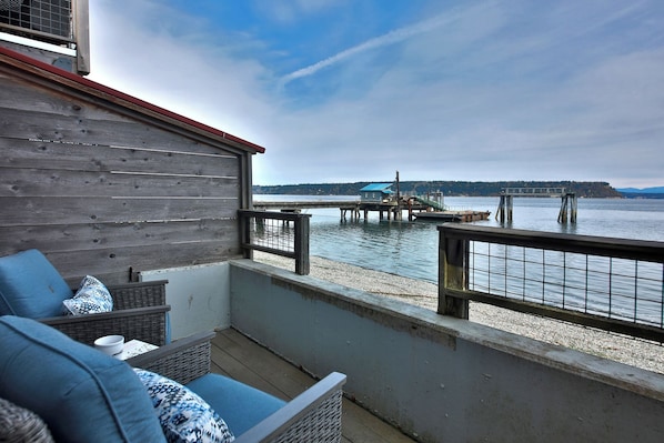 A balcony with wicker furniture, a wooden wall, and a view of a dock and water.
