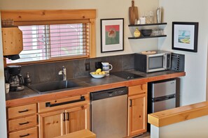 A modern kitchen with a dishwasher, microwave, and a sink. There are wooden cabinets and a window with blinds.