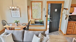 A cozy living room with a sofa, a dining table with chairs, a map on the wall, and a door leading to a kitchen. - Waterfront 1 bedroom condo - private deck offering spectacular views (Langley)