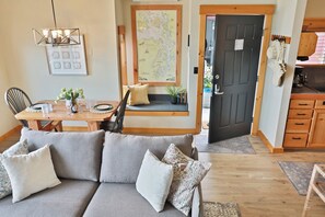 Un salon confortable avec un canapé, une table à manger et des chaises, une carte accrochée au mur et une porte donnant sur la cuisine.