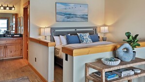 A bedroom with a bed, bedside lamps, a nightstand, a wall-mounted painting, and a view of the kitchen. - Waterfront 1 bedroom condo - private deck offering spectacular views (Langley)