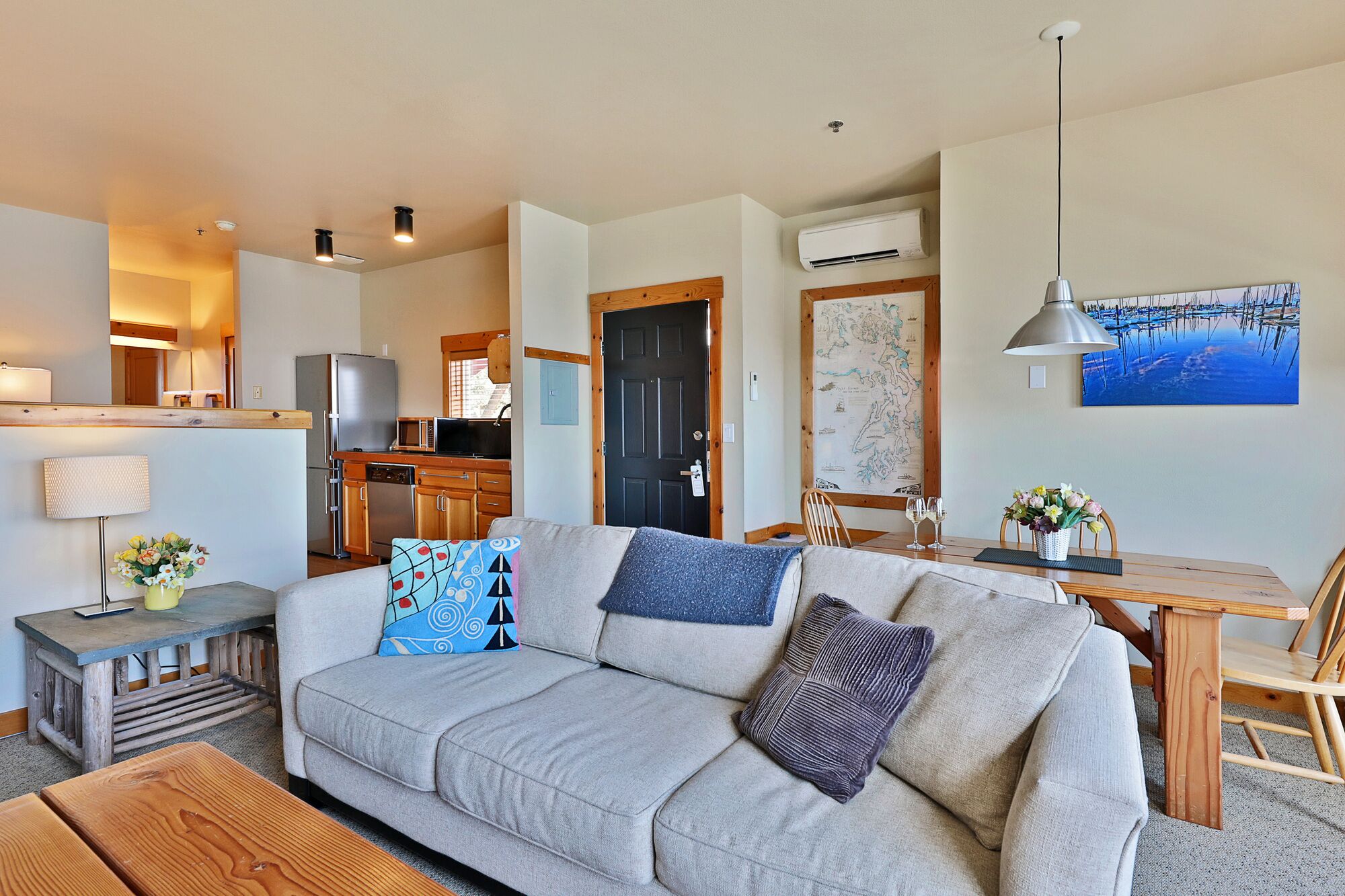 A living room with a sofa, a wooden coffee table, a dining table with chairs, a lamp, and a map on the wall.
