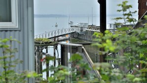 Un muelle que se adentra en aguas tranquilas, con barcos, una estructura de madera y una valla metálica.
