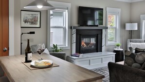 Una sala moderna con chimenea, televisor de pantalla plana y comedor con mesa para dos.