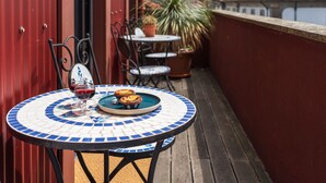 A round table with a blue and white mosaic pattern, a glass of red wine, and two small pastries on a balcony with a red wall and potted plants. - Elegant Duplex Apt in Downtown by Lisbeyond (Porto)