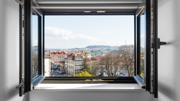 A window with an open view of a cityscape, including buildings and a distant tower. - Elegant Duplex Apt in Downtown by Lisbeyond (Porto)