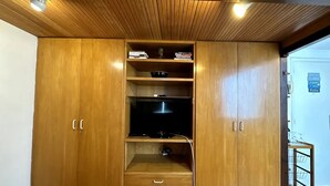 A wooden wardrobe with multiple shelves and drawers, a flat-screen TV, and a small table with a glass top. - Studio Edifício Leblon (Leblon Rio de Janeiro)