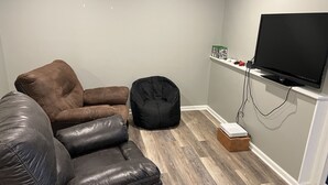 Un salon avec un canapé en cuir marron, un fauteuil en forme de poire noir et un téléviseur à écran plat fixé au mur.