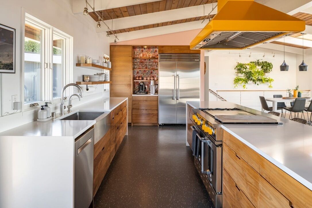 Une cuisine moderne dotée d’un îlot central, d’appareils électroménagers en acier inoxydable, de meubles de rangement en bois et d’un four encastré.