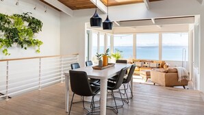 Een moderne eetruimte met een houten tafel en stoelen, een witte balustrade en uitzicht op zee.