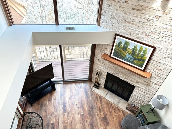 Un salon moderne avec une cheminée en pierre, un tableau accroché au mur et une vue sur une terrasse en bois.