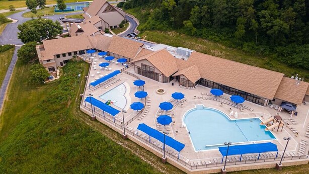 A resort with a large pool area, outdoor seating, and a building with a sloped roof.
