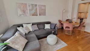 Een moderne woonkamer met een grijze modulaire bank, een ronde salontafel en een eethoek met roze stoelen.