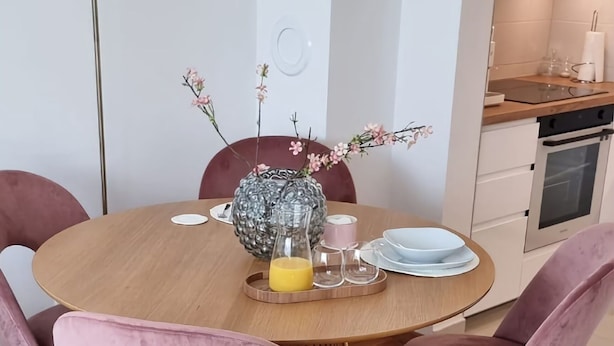 Een moderne eetruimte met een ronde houten tafel, twee roze fluweelstoelen en een vaas met bloemen.