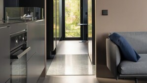 A modern kitchen with a central island, a dining area with a sofa, and a view of greenery through a glass door. - Grend Blefjell (Flesberg)