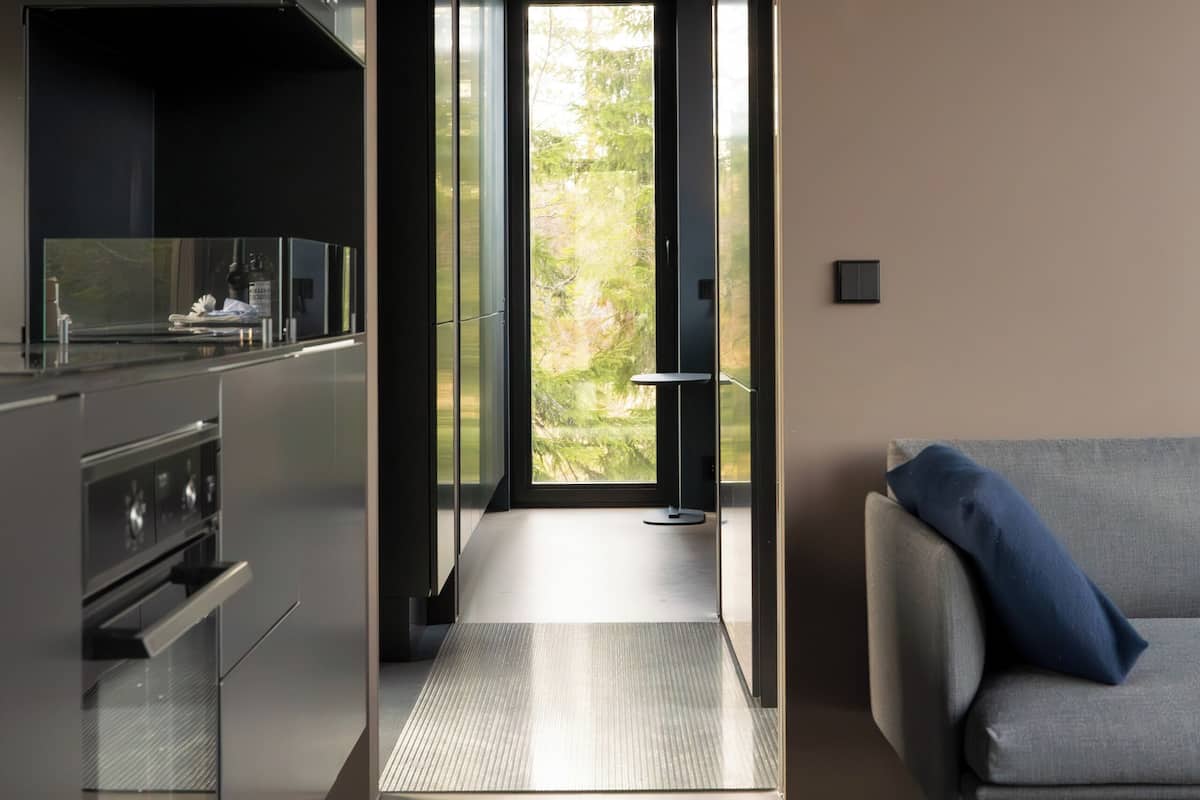 Una cocina moderna con una isla central, un comedor con sofá y vistas a zonas verdes a través de una puerta de cristal.
