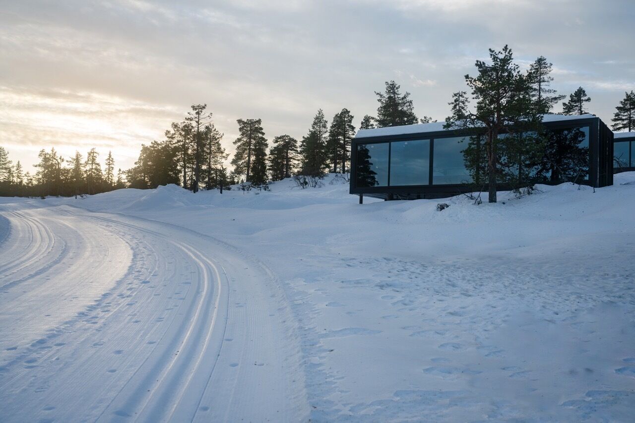 A modern building with large glass windows, surrounded by snow-covered ground and trees.