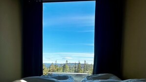 A room with a bed facing a large window, curtains, and a view of trees and mountains. - Grend Blefjell (Flesberg)