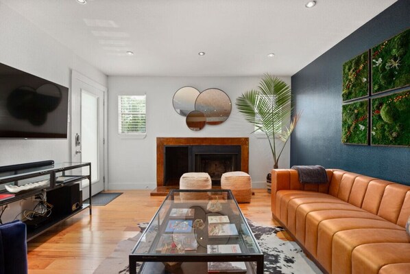 A modern living room with a fireplace, leather sofa, and a coffee table with magazines.