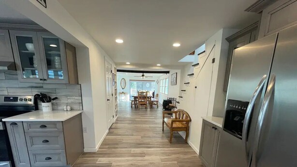 A modern kitchen with a central island, wooden flooring, and a dining area in the background.