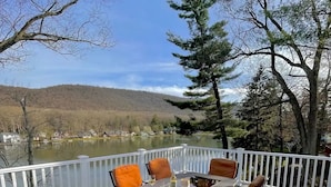 A deck with a table set for four, surrounded by chairs, overlooking a lake and forested hills.
