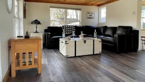 A cozy living room with a wooden ceiling, a black leather sofa, a white storage chest, and a small wooden side table.