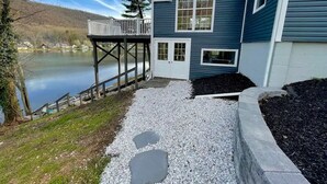 A house with a dock extending over a lake, a gravel driveway, and a small deck.