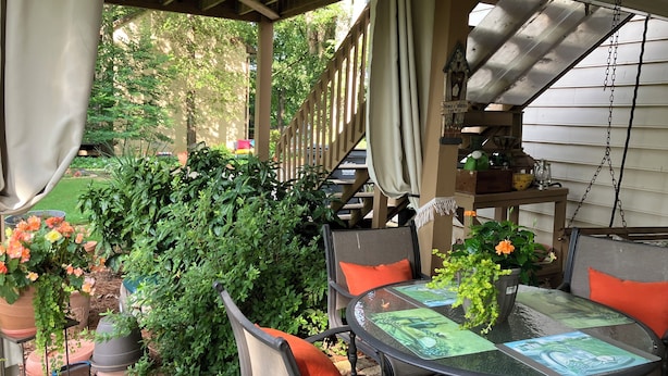 Un patio couvert avec une table et des chaises, entouré de verdure et de plantes en pot.