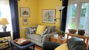 Un salon avec un canapé, un fauteuil en cuir noir, une petite table avec une lampe, une plante en pot et une fenêtre avec des rideaux.