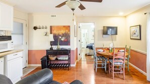 Un salon doté d’un ventilateur de plafond, un coin repas avec une table et des chaises, une cuisine équipée d’un four à micro-ondes et un couloir menant à une autre pièce.