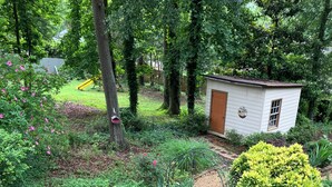 Un jardin avec un chemin bordé de pierres rouges, diverses plantes et un petit abri de jardin.
