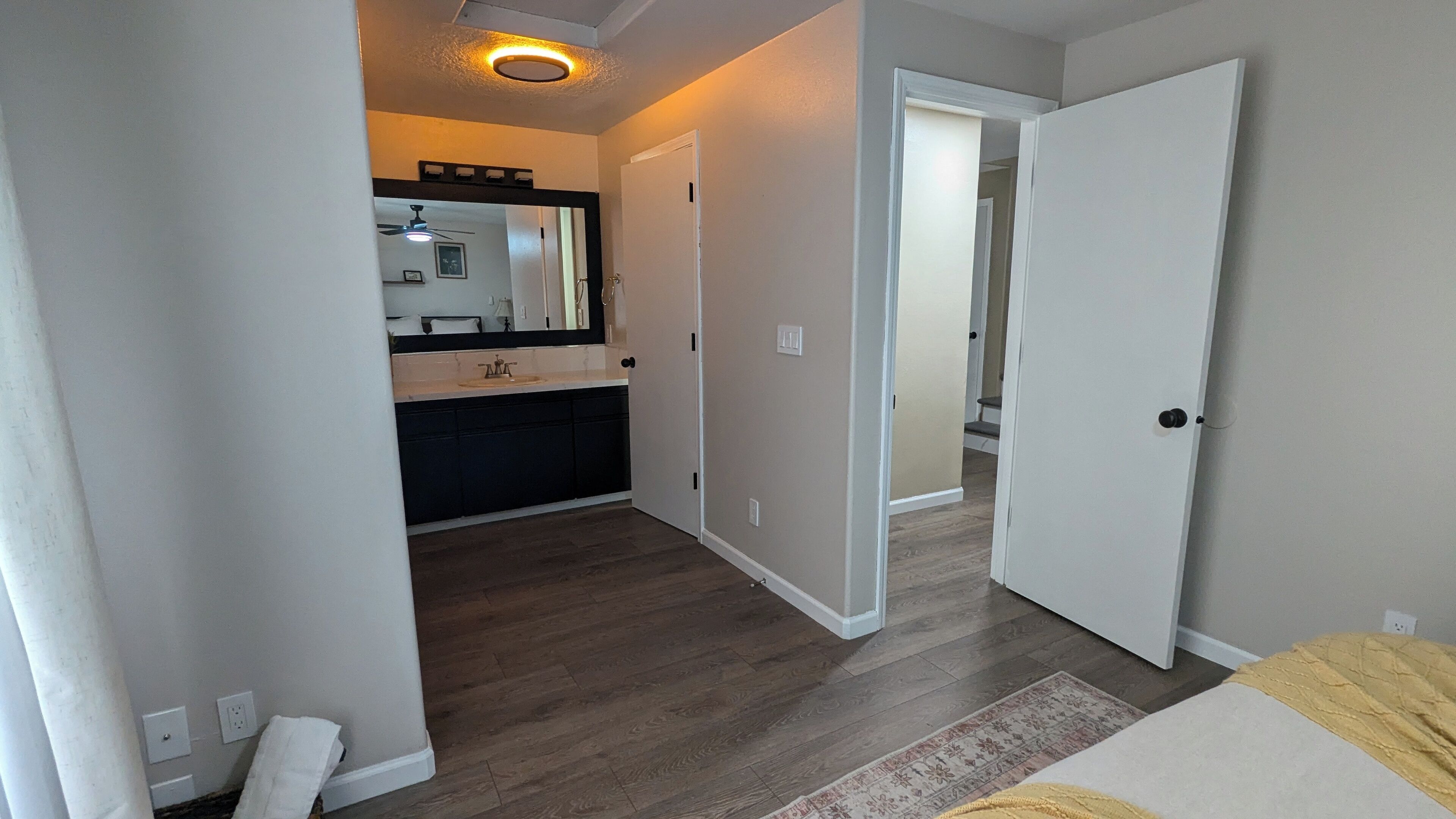 Une chambre à coucher comprenant un lit, une table de chevet et une porte donnant sur une salle de bain avec un lavabo et un miroir.