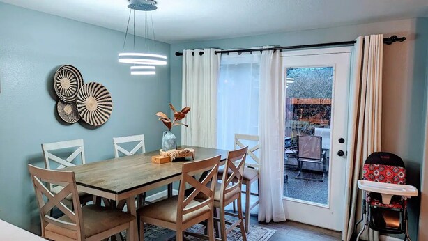 A dining area with a wooden table and chairs, a vase with dried flowers, and wall art.