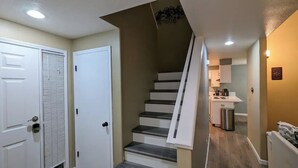 A staircase leading to a second floor, a kitchen area with cabinets and appliances, and a white door with a window.