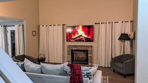A living room with a fireplace, a television mounted above it, and two sofas.
