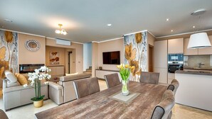 A modern living room with a dining table, sofas, and a kitchen area.