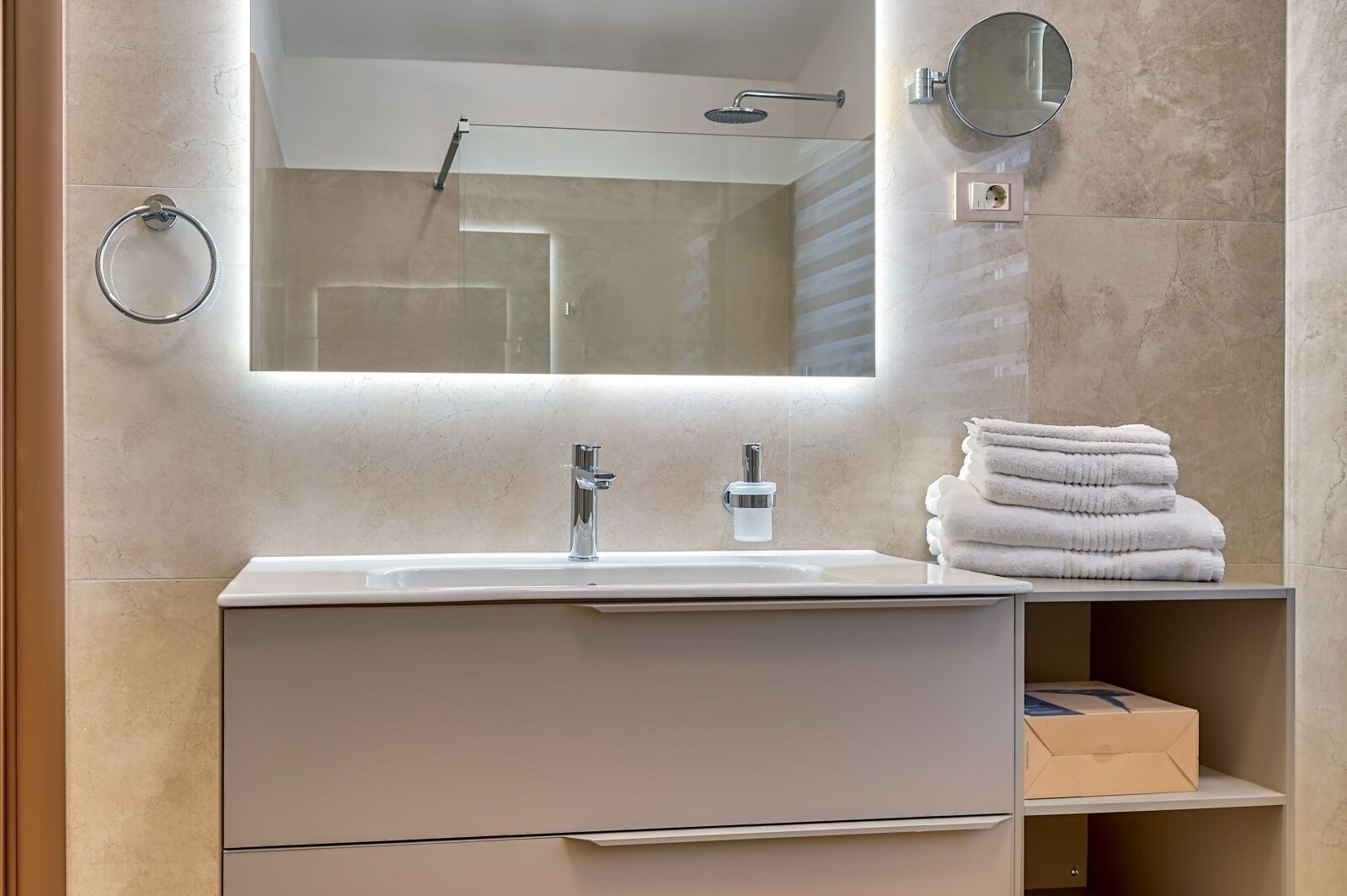 A modern bathroom with a large mirror, a sink with a faucet, and a stack of towels on a shelf.