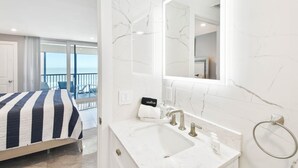 Ein Hotelzimmer mit Bett, Badezimmer mit großem Spiegel, Waschbecken und Blick auf den Balkon.