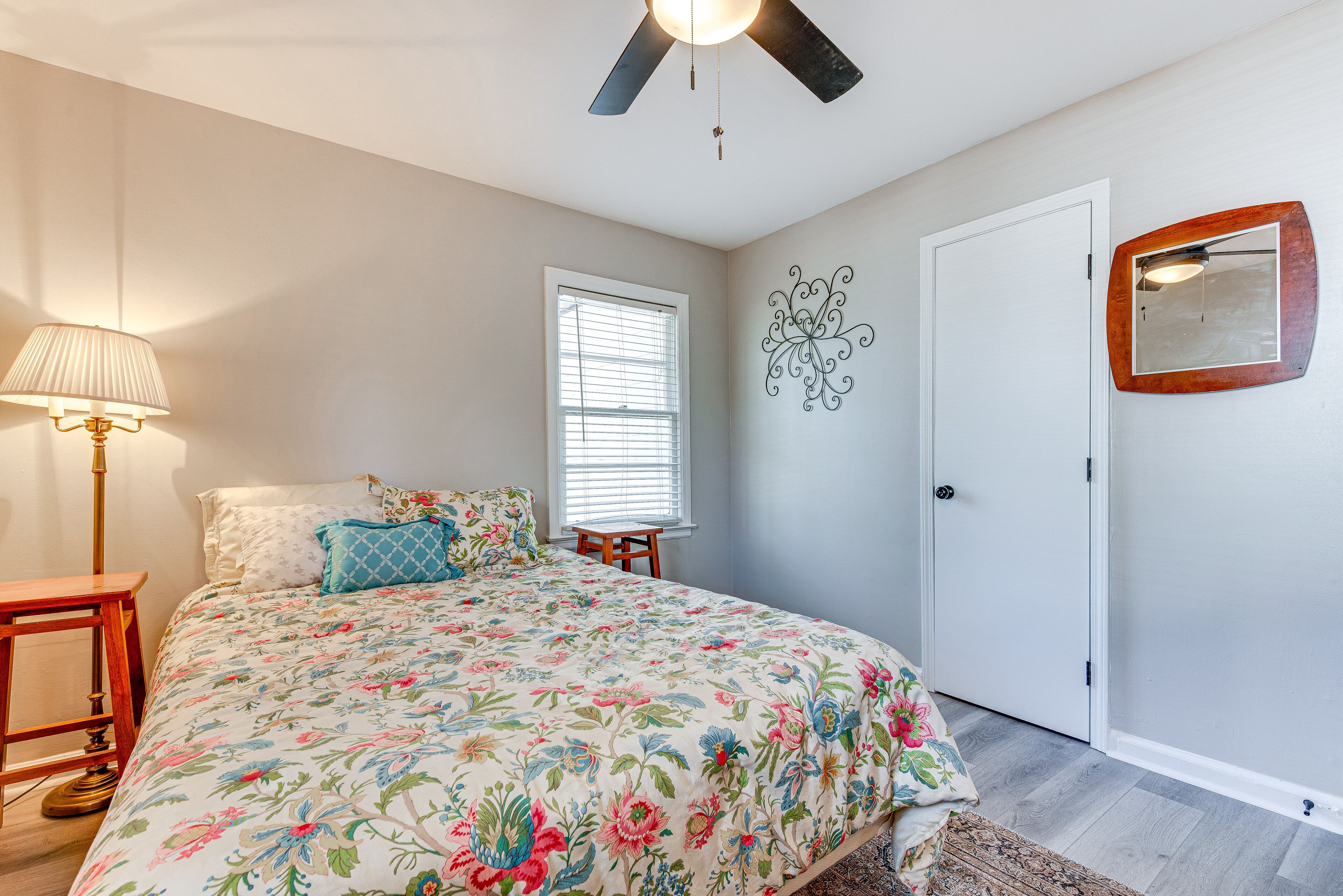 Une chambre à coucher comprenant un lit, un ventilateur de plafond, une fenêtre, une porte et un miroir fixé au mur.