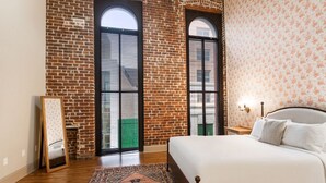 A bedroom with a large bed, a brick wall, and two windows with shutters. - Hidden Gem – Steps to French Quarter Food & FunHistoric Charm: Walk to Bourbon/French Quarter (Room in a Hotel) (New Orleans)