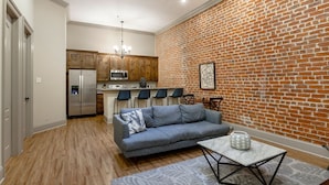 A modern kitchen with a brick wall, a grey sofa, and a dining table with chairs.