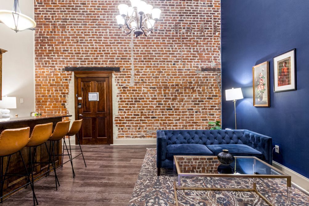 A room with a brick wall, a blue sofa, a glass coffee table, and a bar area with stools.