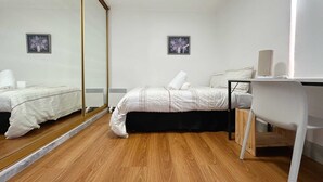 Une chambre avec deux lits, un plancher en bois, un bureau et un miroir.