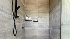 Une douche équipée d’un pommeau de douche à main, d’un tuyau noir et d’une étagère pour les articles de toilette.