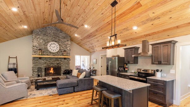 A spacious kitchen with a stone fireplace, wooden ceiling, and modern appliances.