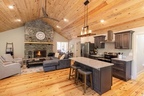 A spacious kitchen with a stone fireplace, wooden ceiling, and modern appliances.