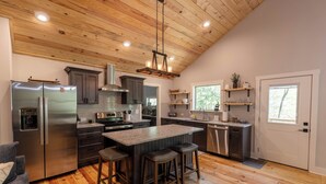 A modern kitchen with a central island, stainless steel appliances, wooden flooring, and a vaulted ceiling.