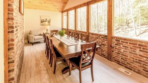 A wooden dining table with chairs, a sofa, and a window with a forest view.